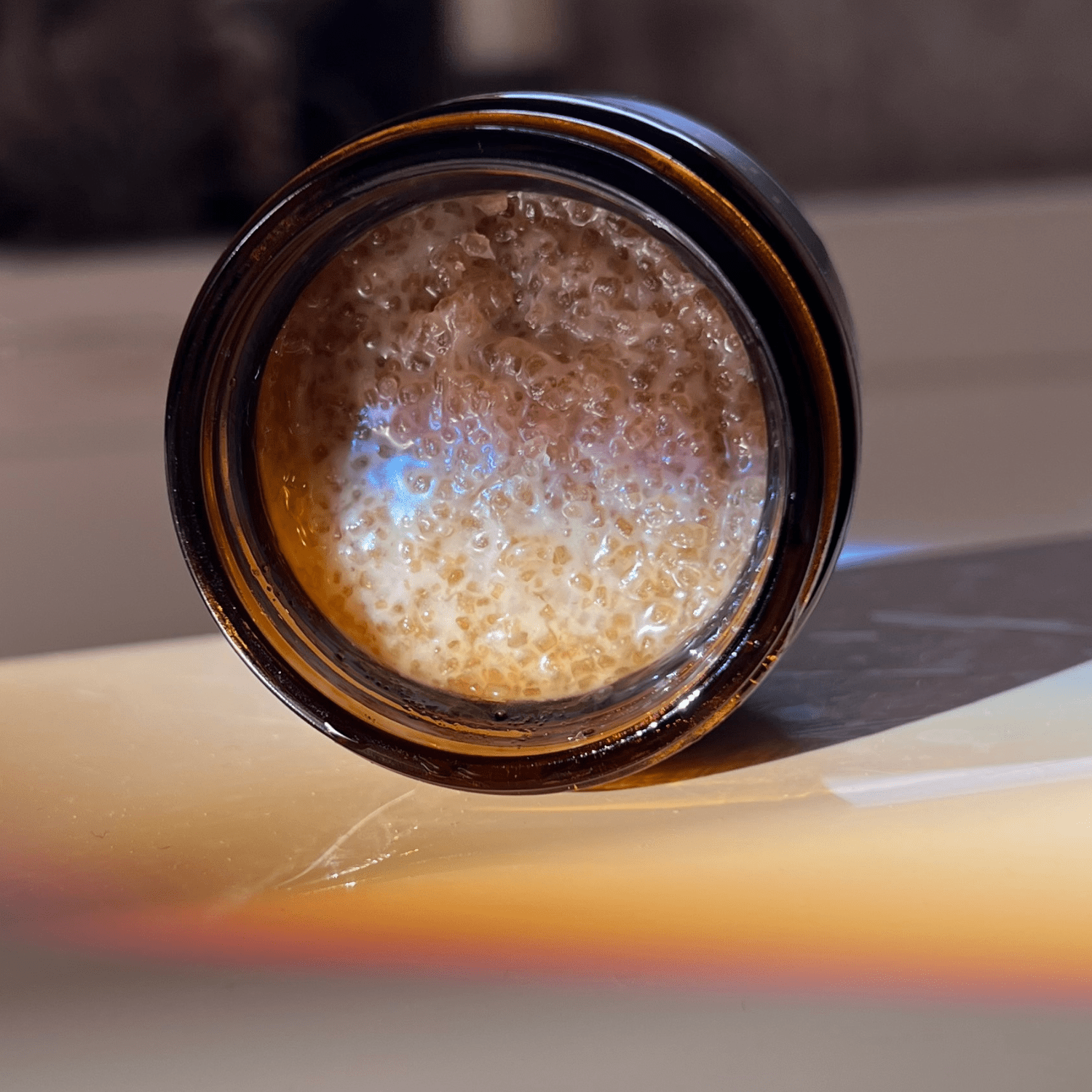 Close-up of a brown glass jar with a black lid on a reflective surface.